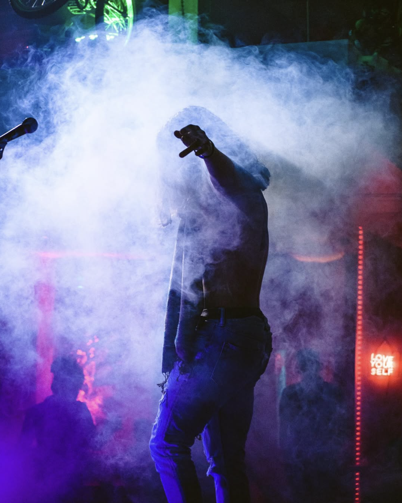 Silhouette of Jourdan Blue on a smoke-filled stage with his arm raised